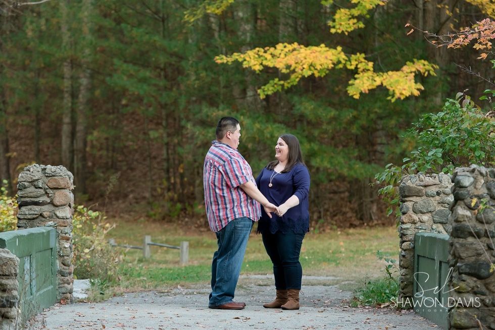 Two people holding hands on a stone path in a wooded park, smiling at each other.