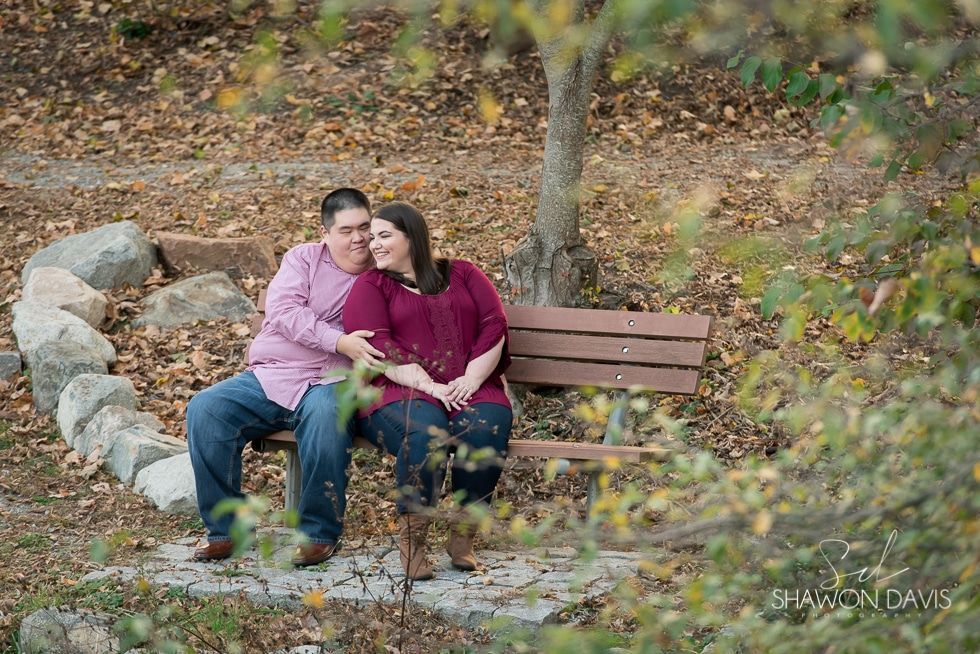 Couple sitting on a park bench, leaning together in an autumn setting.