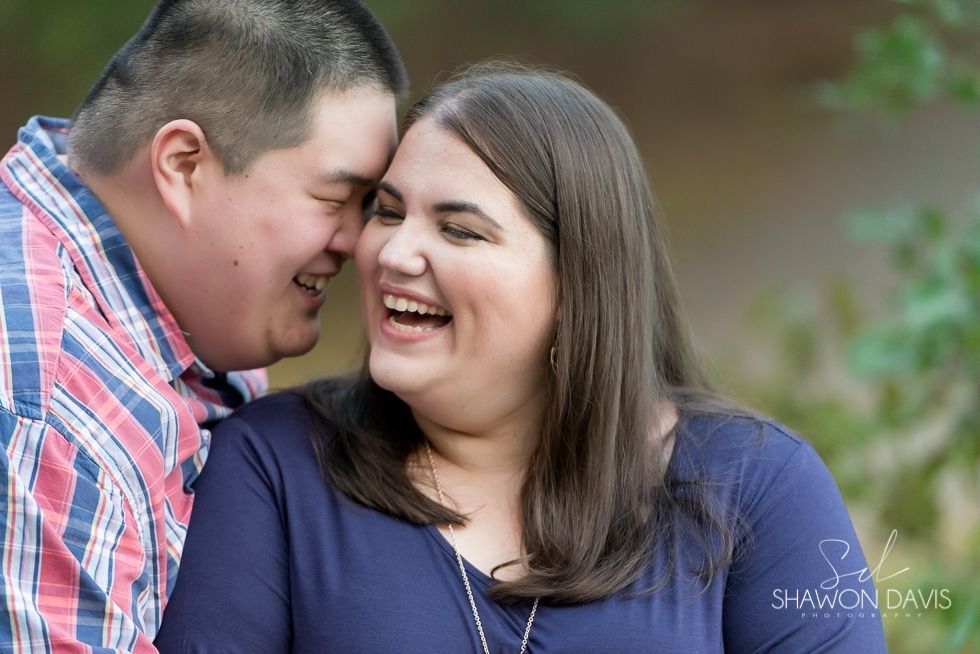 Two people smiling and touching foreheads outdoors, with a blurred green background.