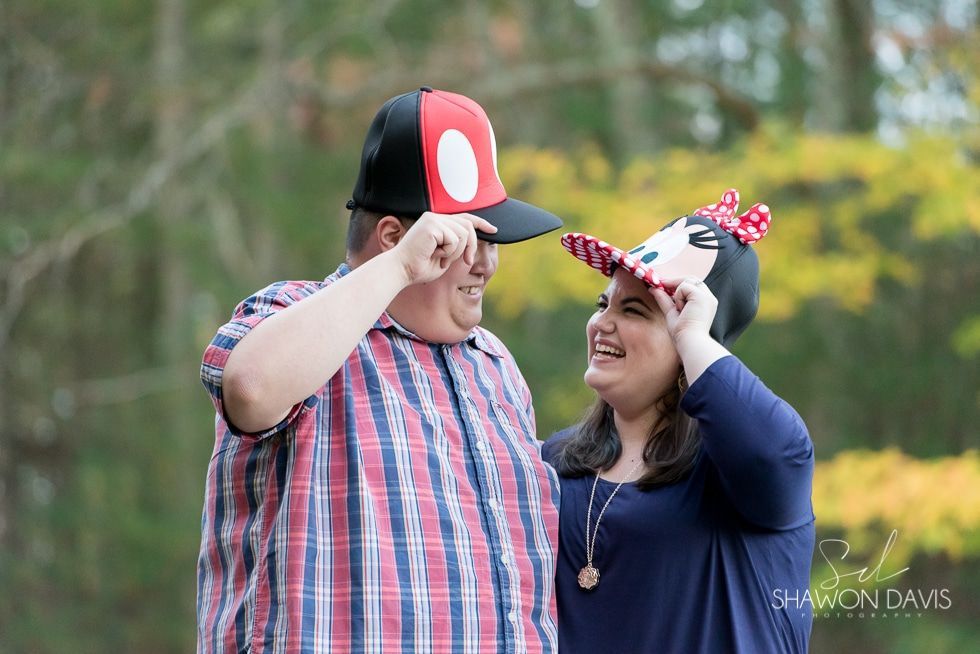 Couple in matching hats smiling and adjusting them outdoors in a grassy field