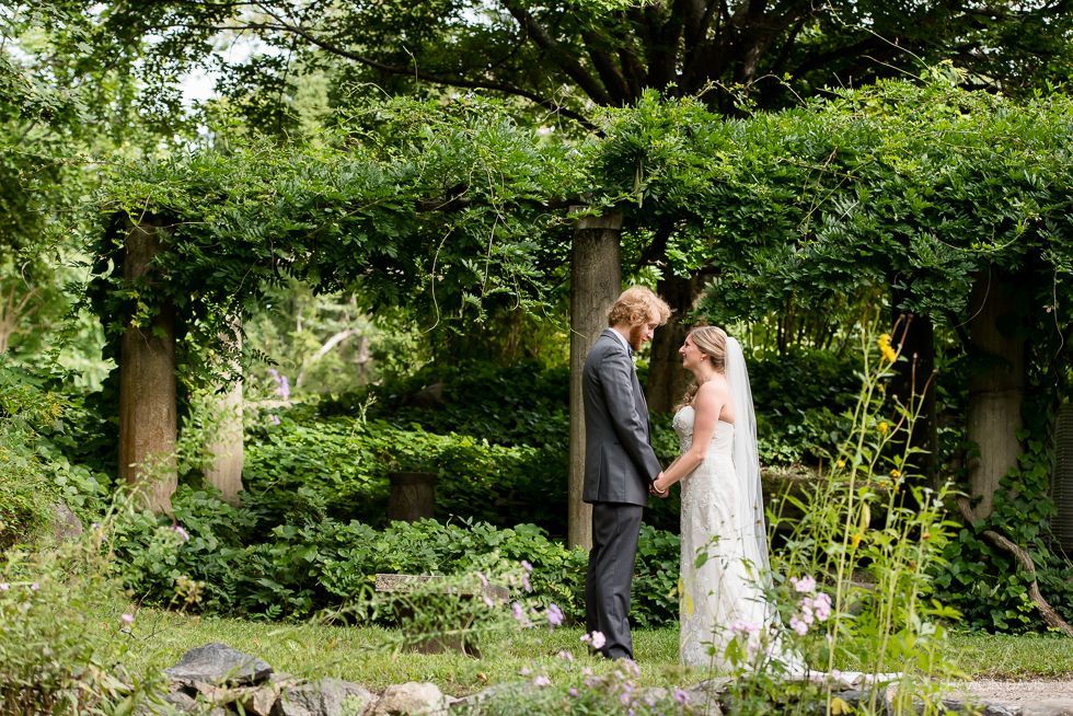 Bride and groom holding hands in a lush garden wedding arch, surrounded by greenery