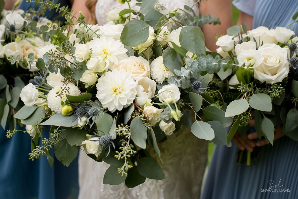 White floral bouquets with greenery held by people in blue dresses