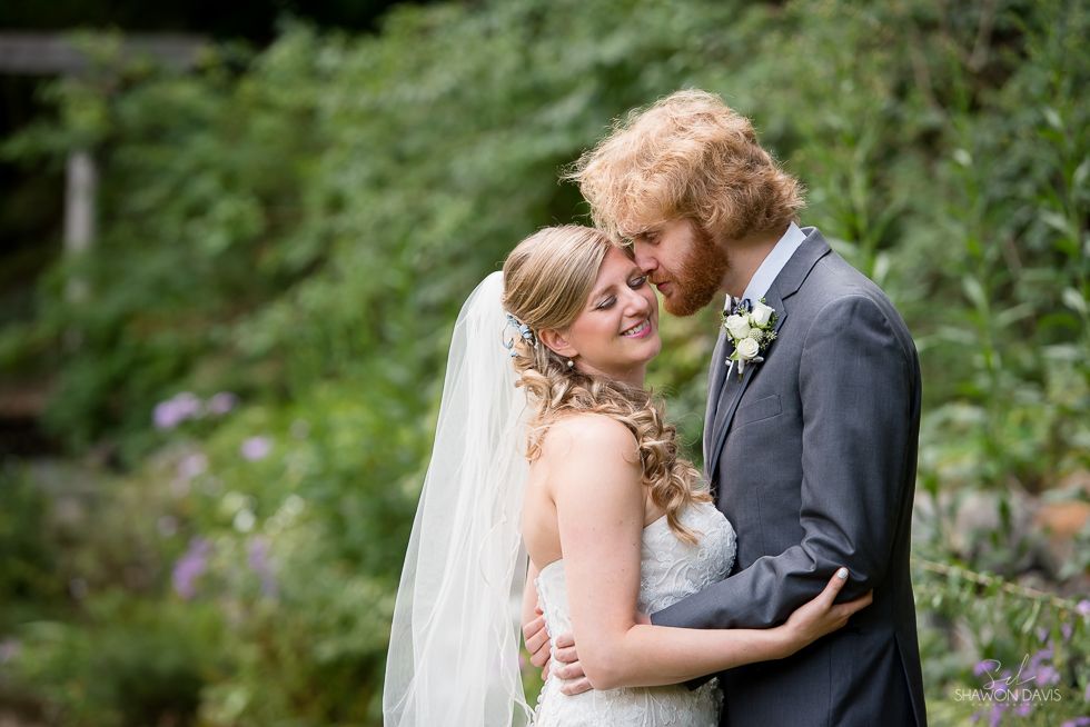 Bride and groom embracing outdoors in a lush garden, sharing a close, tender moment.
