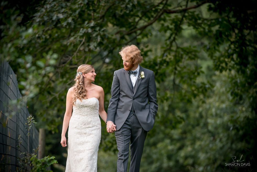 Bride and groom in formal wear walking hand in hand under green trees