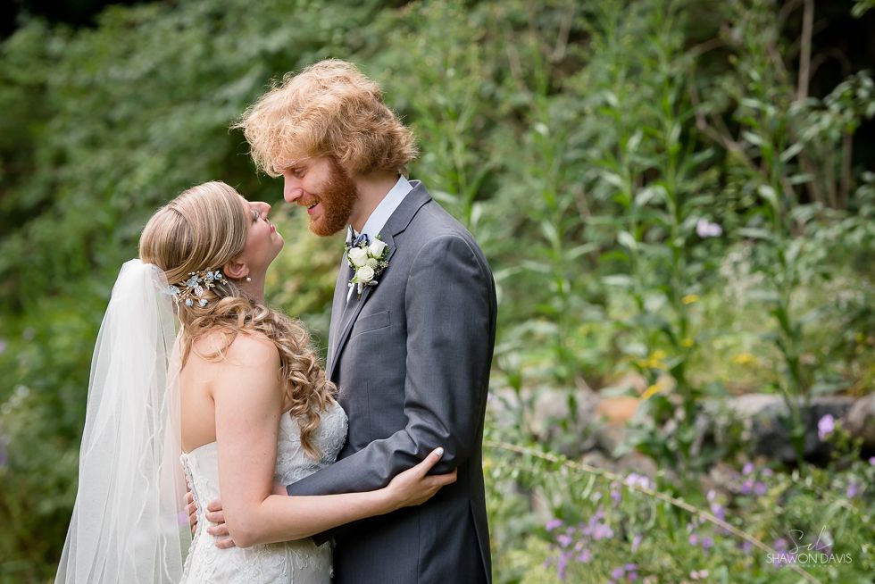 Bride and groom embracing in a green garden, smiling at each other during a wedding ceremony.