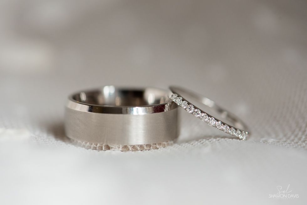 Two silver wedding bands on a soft white fabric background, one upright and one leaning with diamonds.