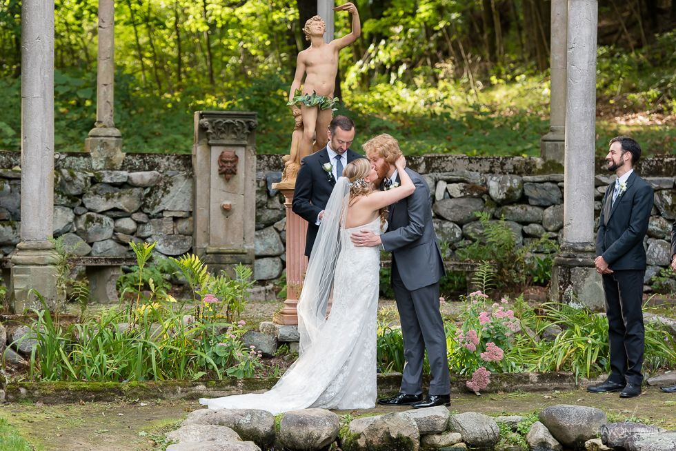 Wedding couple kissing outdoors in front of a stone fountain and garden statue
