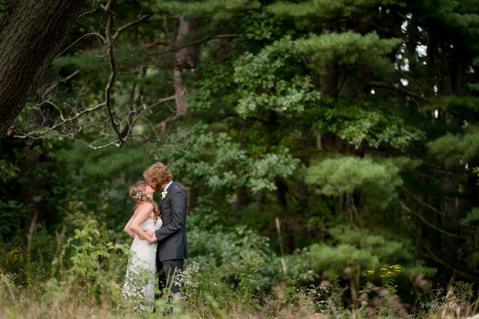 Couple embracing in a lush green forest, the bride in white and groom in a dark suit.