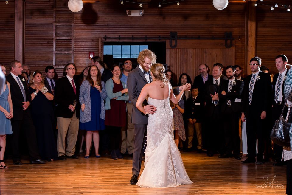 Bride and groom slow-dancing at a wedding reception, surrounded by guests in a wood-paneled hall