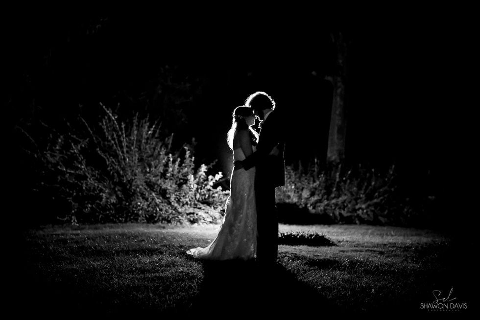 Couple embracing in a dark, black-and-white outdoor scene, backlit and silhouetted at night
