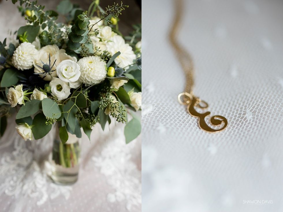 White bridal bouquet beside a gold infinity pendant on a white textured surface