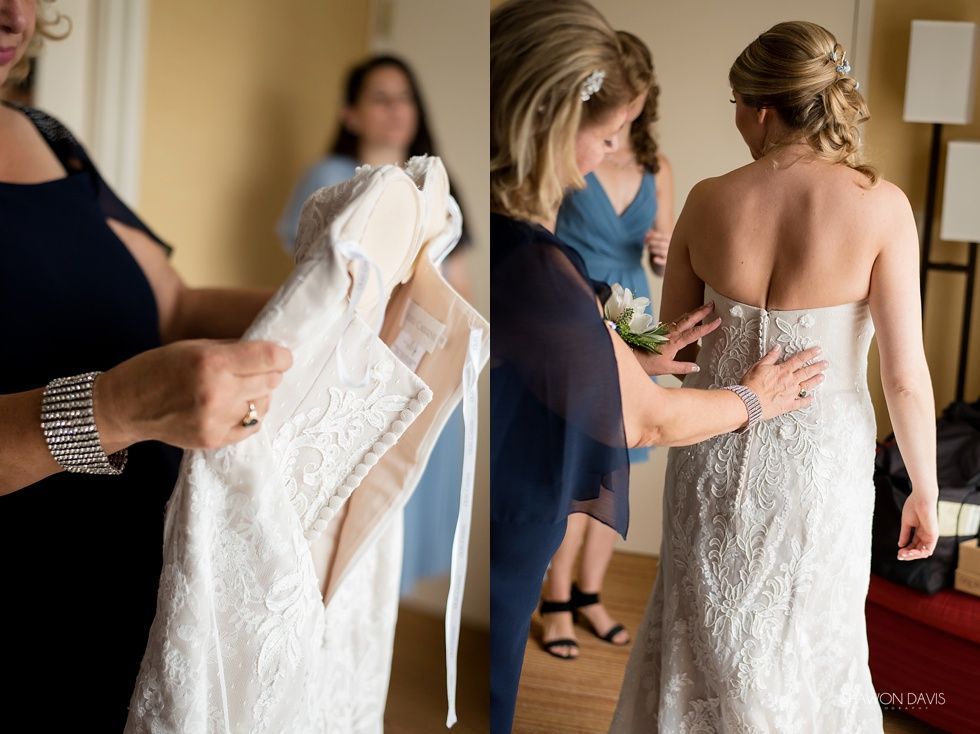 Women in a dressing room examining dresses, including a white gown and a backless beige dress.