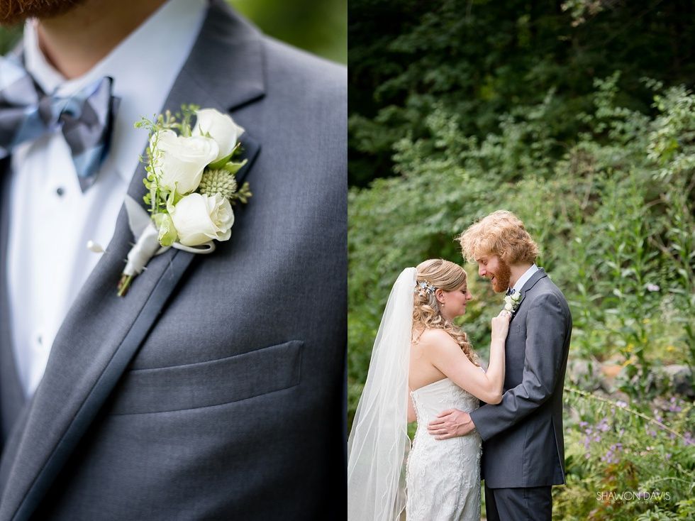 Wedding couple embracing outdoors; groom’s gray suit and white boutonniere in foreground.