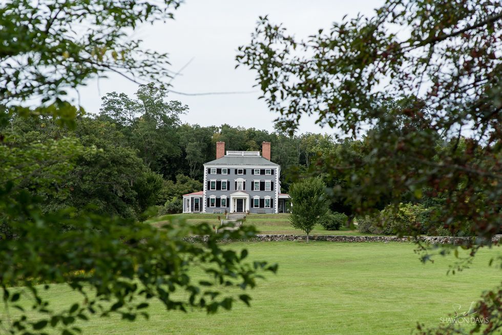 White mansion with red chimneys behind green lawn and trees