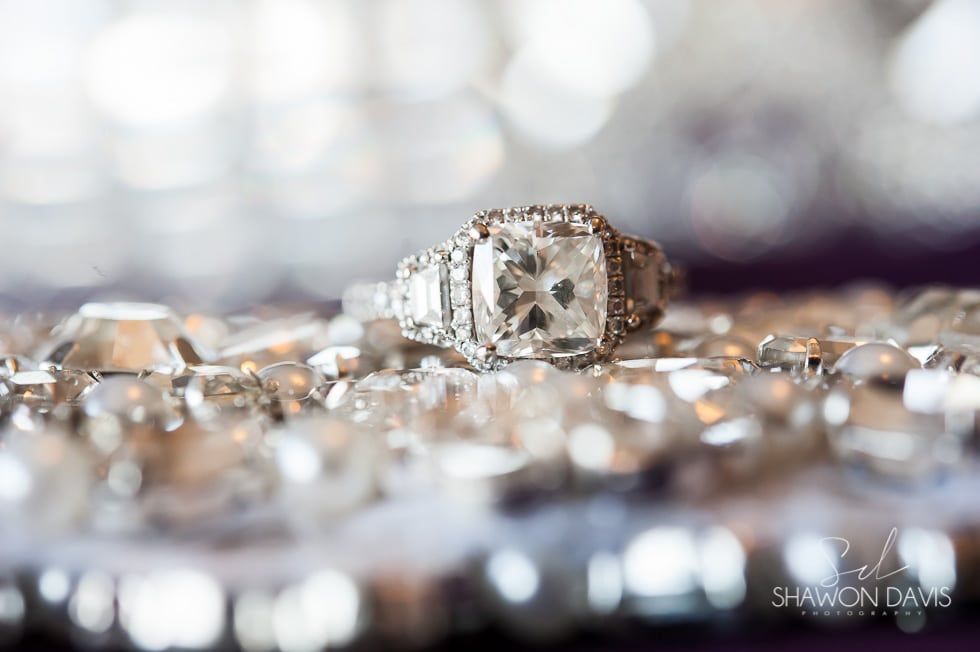 Diamond engagement ring on a crystal-studded surface with soft blurred lights in the background
