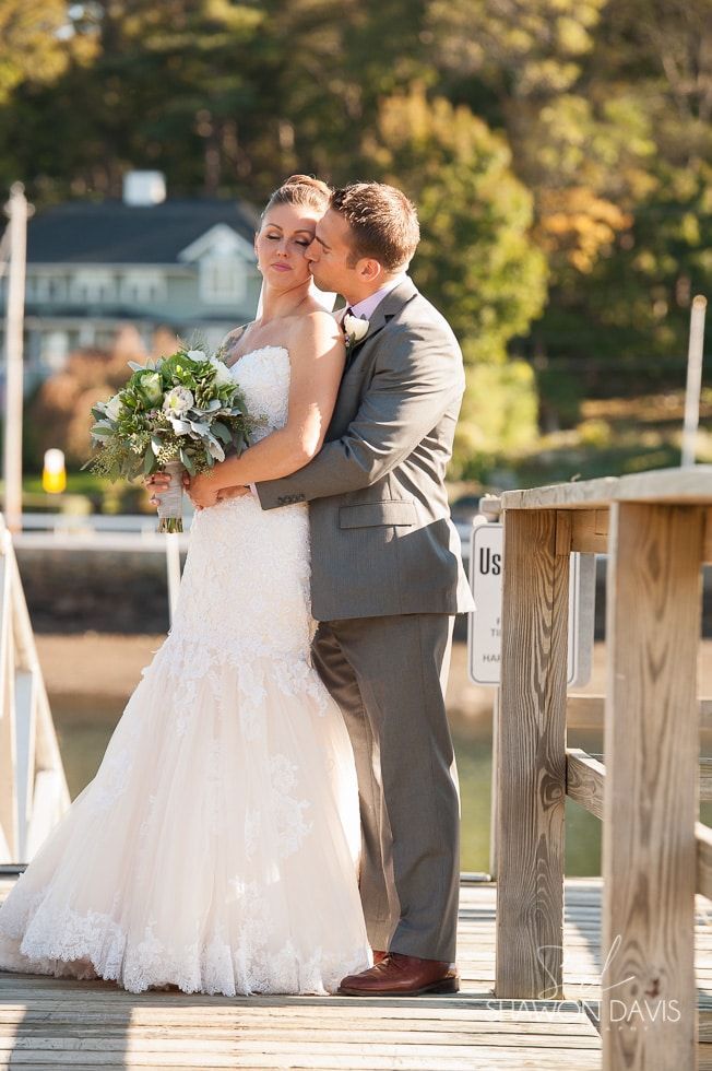 Bride and groom embracing on a dock, with the bride in a white dress holding a bouquet.