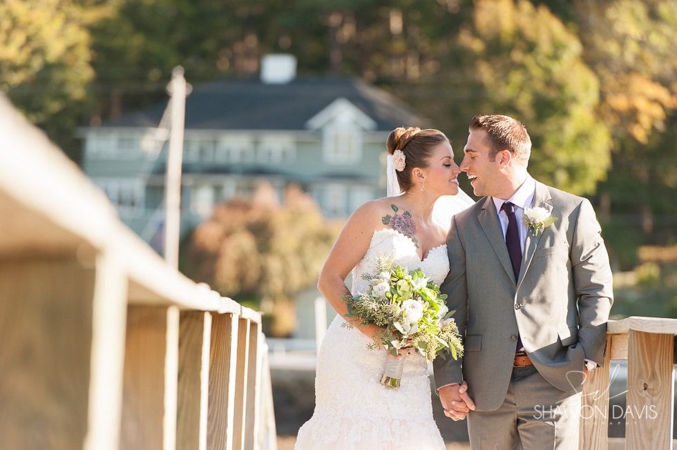 Bride and groom kissing on a wooden bridge, with bouquet and soft-focus houses in the background