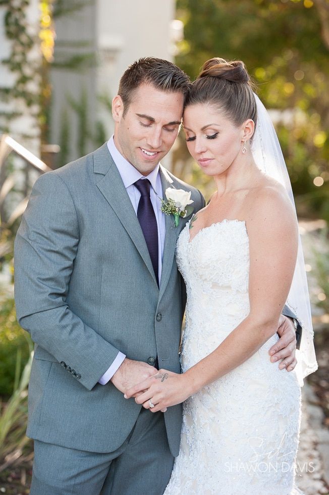 Bride and groom standing together outdoors, holding hands and looking down at their wedding rings.