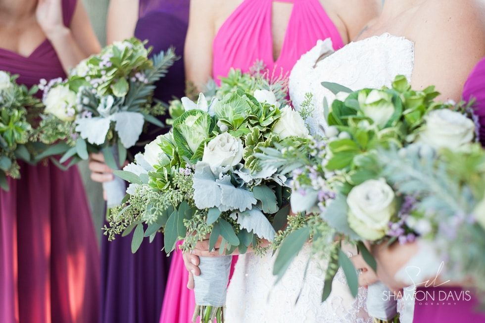 Bridesmaids holding lush white and green bouquets with pink dresses in a wedding setting