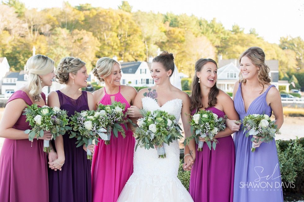 Bride with five bridesmaids in magenta dresses holding bouquets outdoors at a wedding.