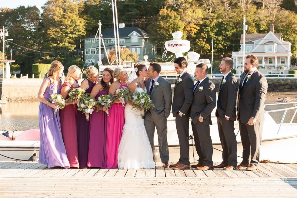 Wedding party posing on a dock, with bridesmaids in purple, bride in white, and groomsmen in dark suits.