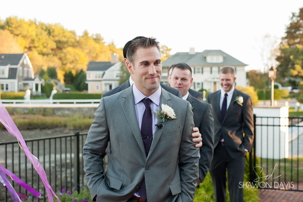 Man in gray suit walking outdoors with two men behind him near a waterfront at sunset