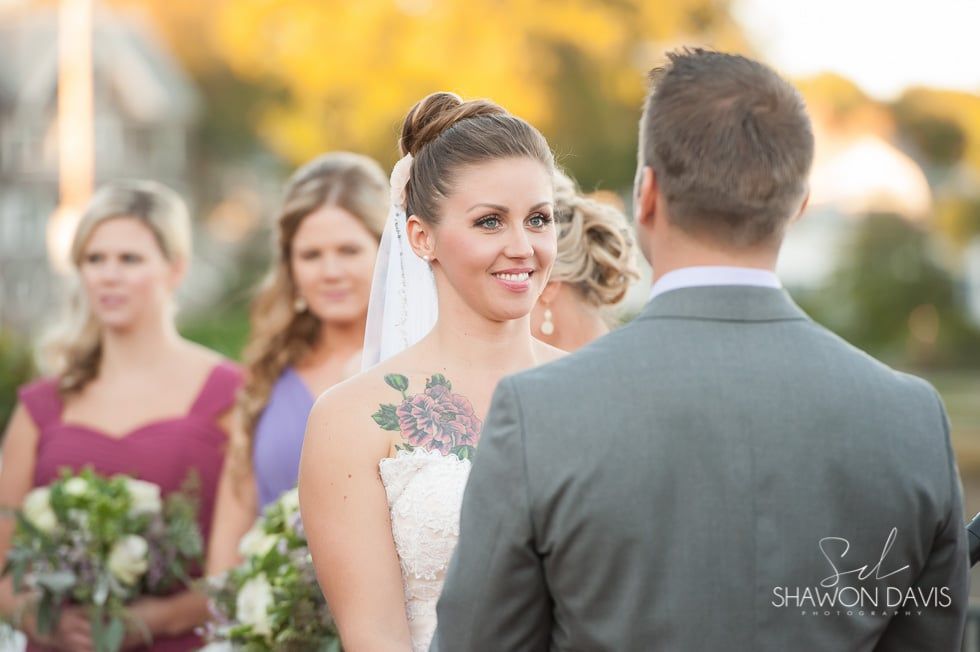 Bride smiling at groom during outdoor wedding ceremony, bridesmaids blurred in the background