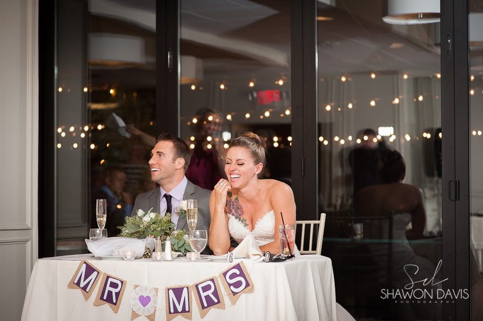 Bride and groom seated at a decorated wedding reception table, smiling with a “Mr & Mrs” banner.