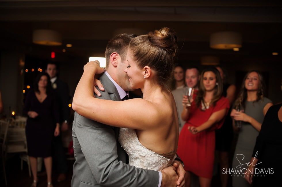 Couple sharing a kiss on the dance floor at a wedding reception, with guests watching in the background