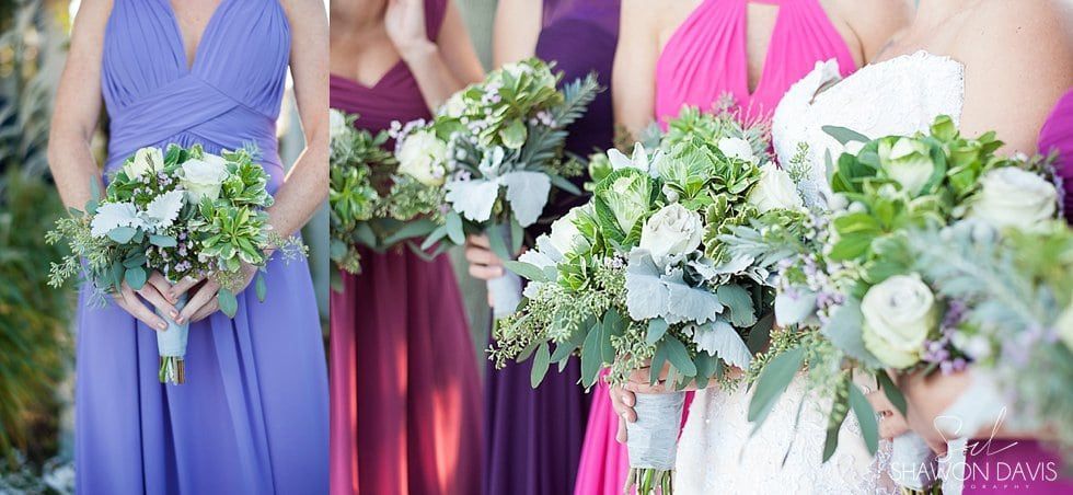Bridesmaids holding white-and-green bouquets in purple and burgundy dresses beside a bride in white