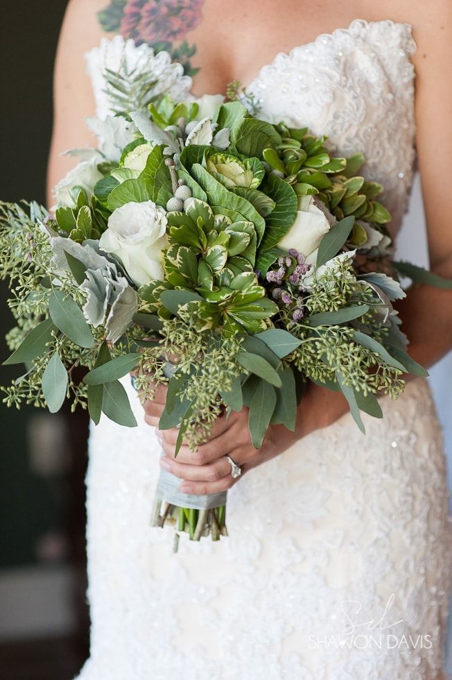 Bride holding a lush green and white bouquet in a lace wedding dress