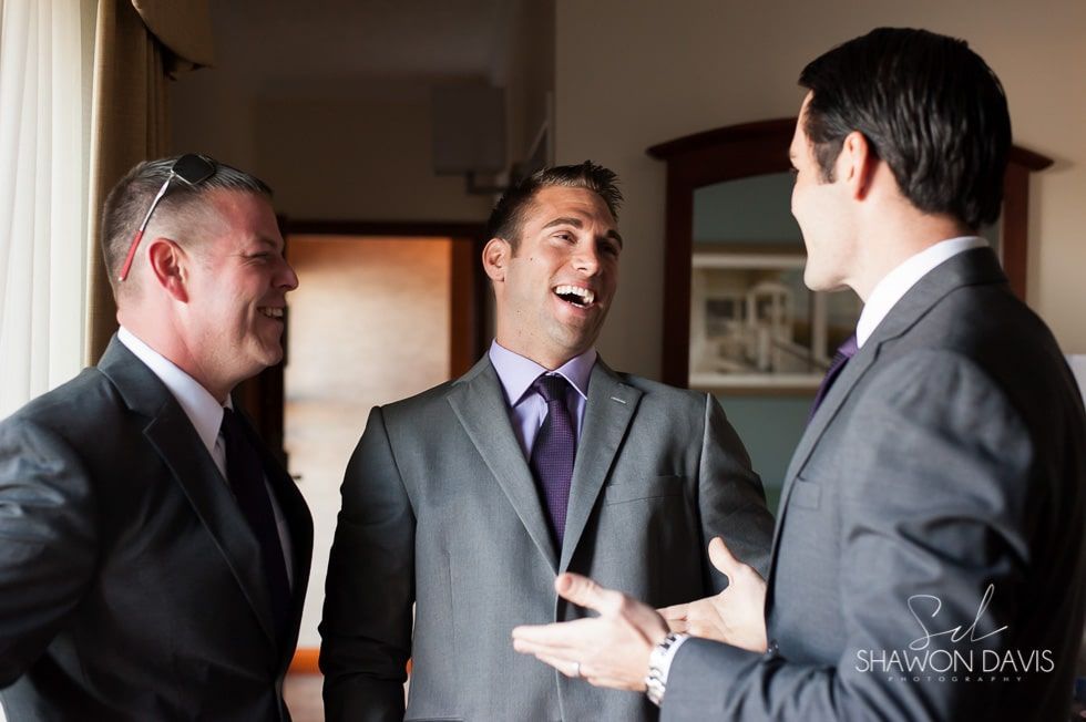 Three men in suits chatting and smiling in a hallway or doorway.