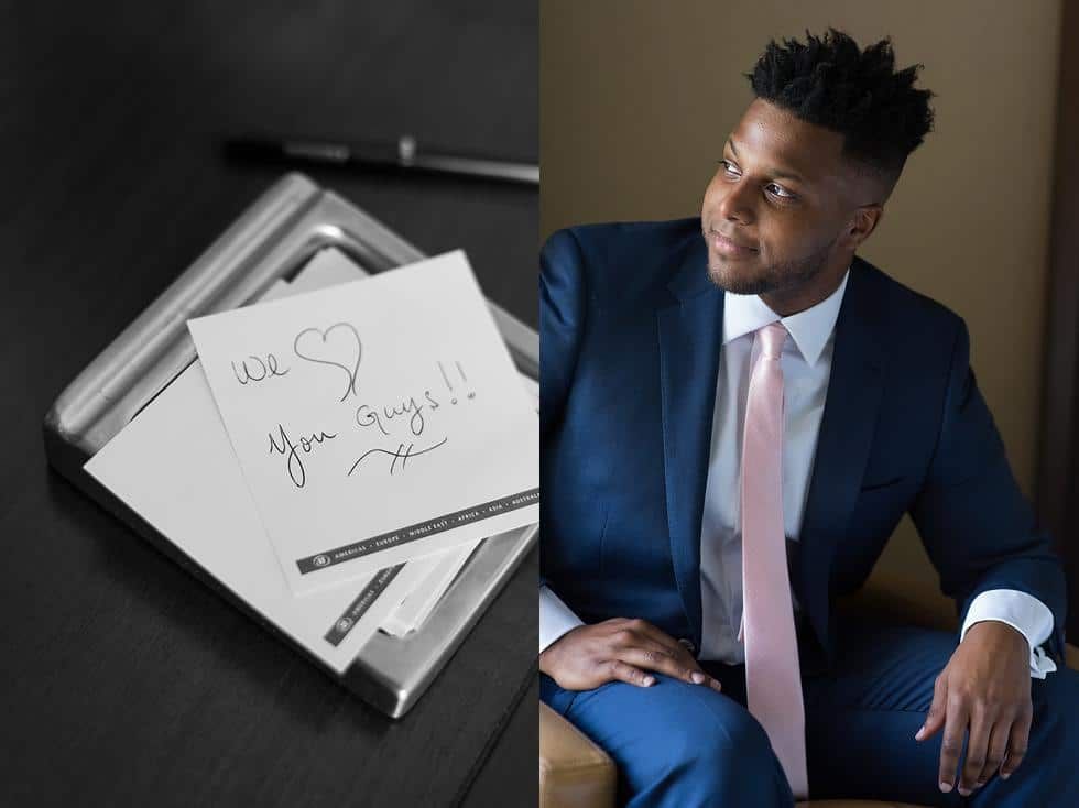 Man in navy suit and pink tie seated beside open gift box with handwritten note and paper heart