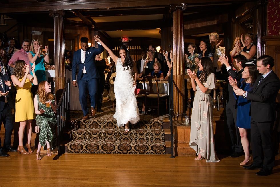 Bride and groom entering a reception hall as guests cheer and clap from both sides