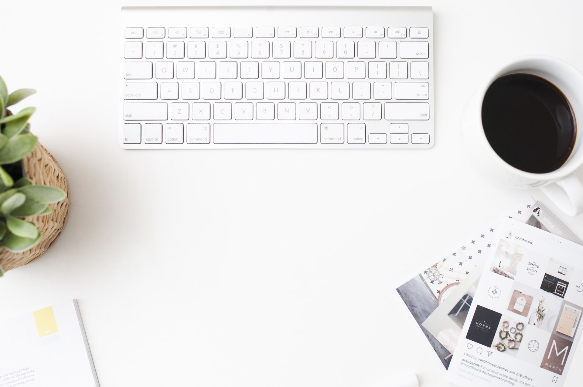 Minimal white desk with keyboard, coffee, plant, and papers on a clean workspace
