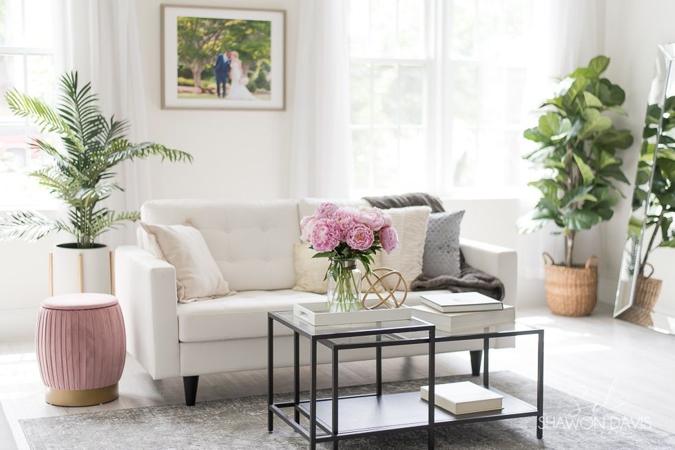 Bright living room with white sofa, coffee table, flowers, plants, and sunlight from large windows