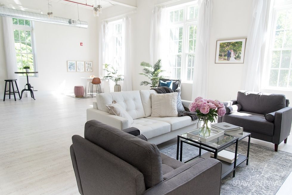 Bright living room with white walls, gray sofas, a glass coffee table, and large windows with natural light