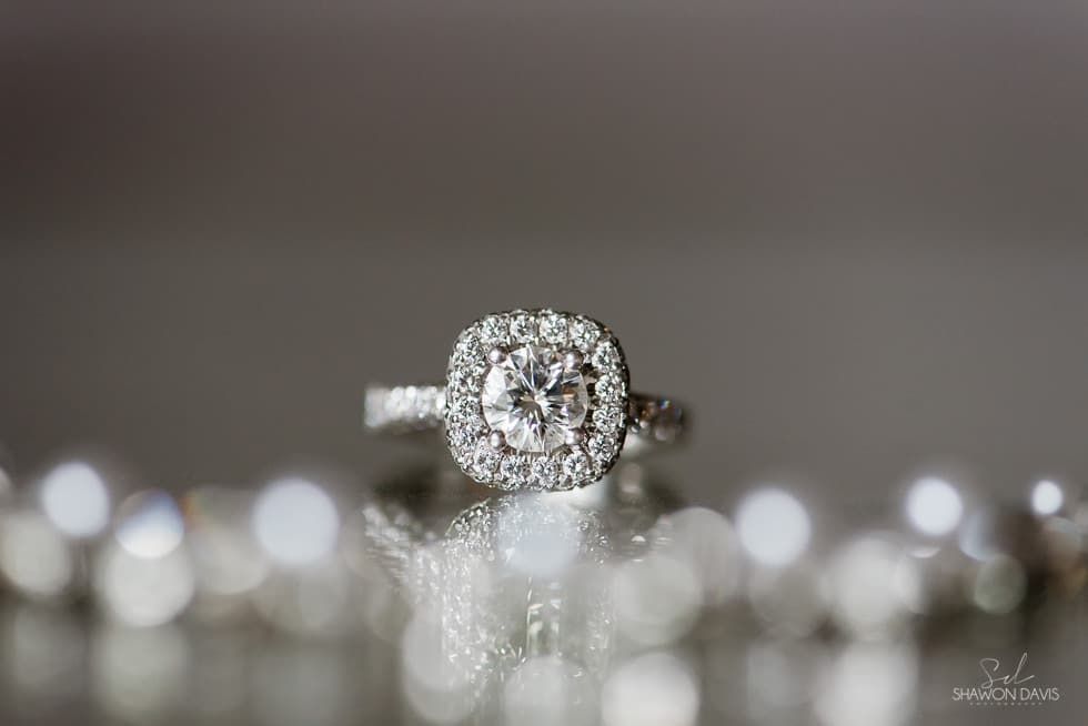 Diamond engagement ring on a reflective surface with blurred lights in the background