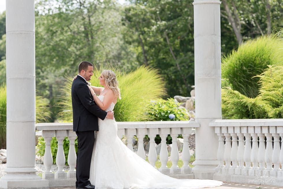 Bride and groom embracing on a white gazebo porch with greenery in the background