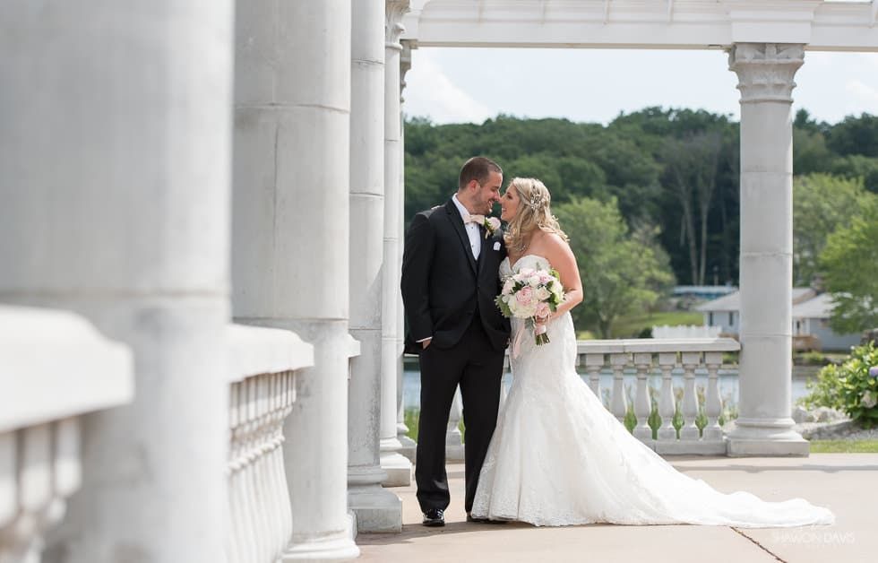 Bride and groom sharing a kiss on a white-column terrace with greenery in the background