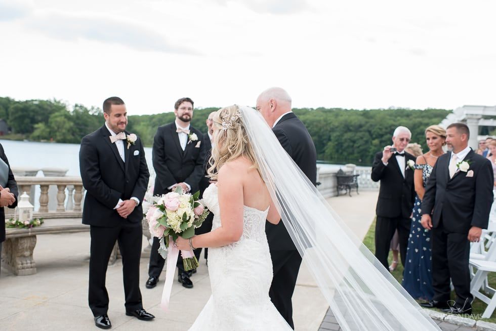 Wedding party outdoors on a bridge, bride holding bouquet and groom waiting with officiant and groomsmen nearby