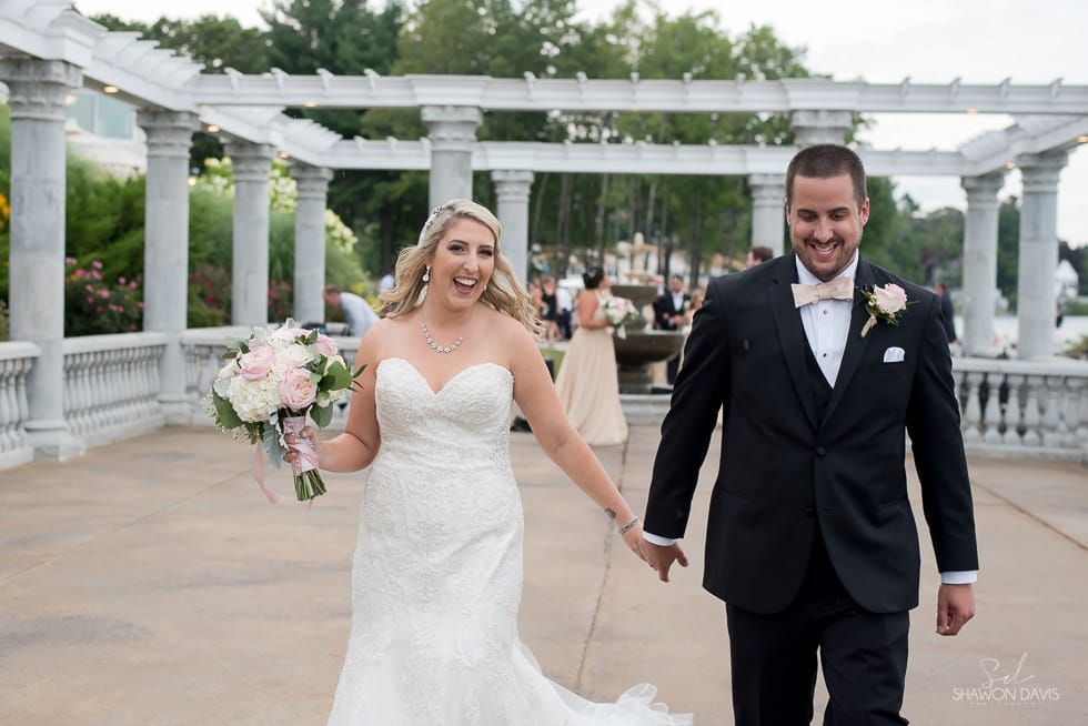 Bride and groom holding hands and smiling on a white pergola walkway outdoors