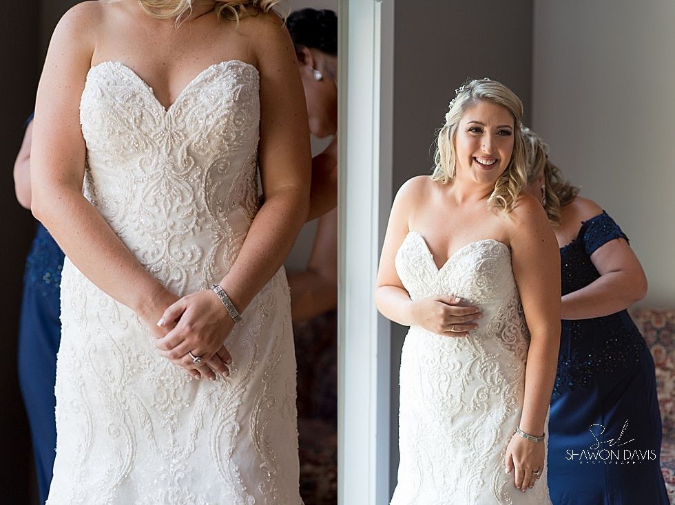 Bride in a white strapless lace gown, smiling and adjusting her dress with others behind her.