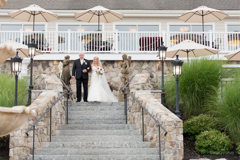 Bride and groom descending stone steps outside a patio venue with umbrellas and lanterns