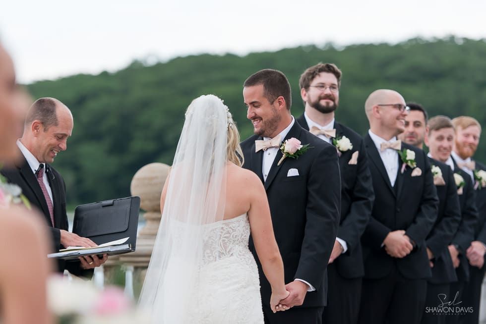 Bride and groom holding hands during an outdoor wedding ceremony, with groomsmen standing nearby
