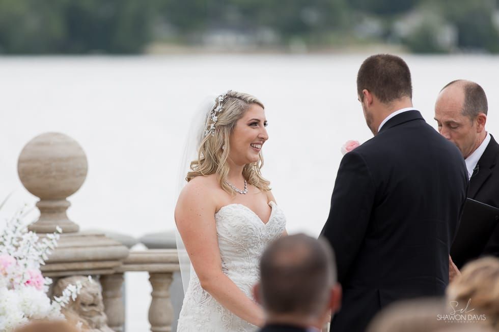 Bride and groom facing each other during an outdoor wedding ceremony by the water