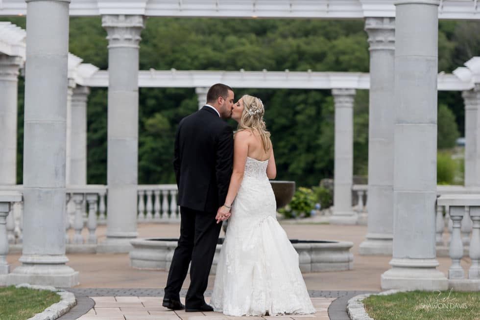Bride and groom standing together under a white stone pergola in a garden courtyard