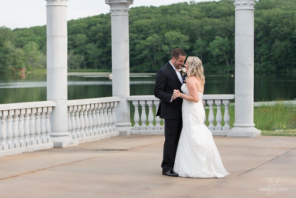 Bride and groom embracing on a white-columned lakeside terrace