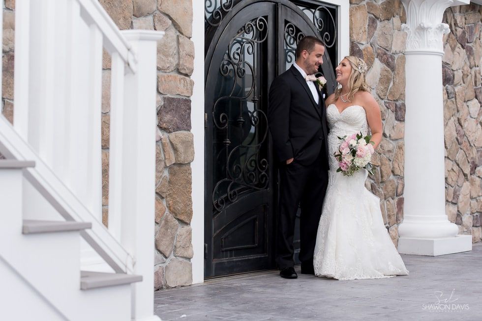 Bride and groom posing in wedding attire by an ornate black doorway with stone walls and white columns