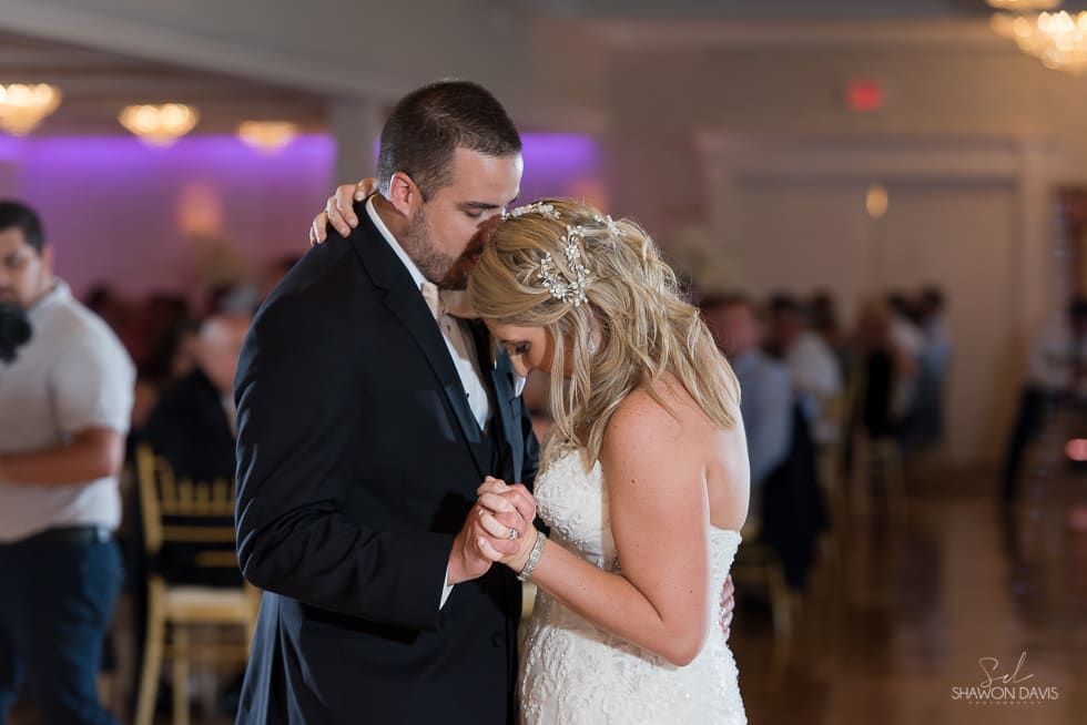 Couple dancing closely at a dimly lit reception, holding hands in formal attire.